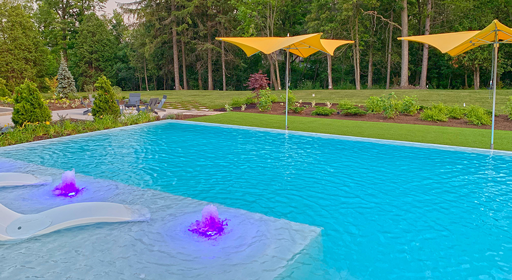 Backyard infinity pool at a private residence with a tanning ledge, geysers with colour lights, and shade umbrellas